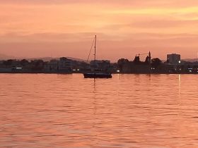 A serene sunset view featuring a sailboat anchored in calm waters, creating a picturesque scene perfect for evening relaxation.