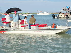 A lively group enjoys a day on the water aboard a fishing boat, complete with drinks and an umbrella for shade — perfect for a fun day out on the water.