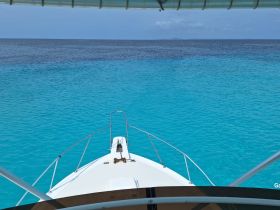 A stunning view from the front of a yacht cruising through crystal-clear turquoise waters, perfect for exploring beautiful marine destinations.