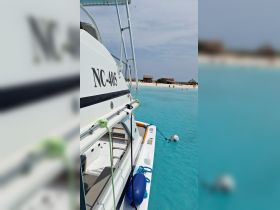 A close-up view of the NC-405 boat anchored in crystal-clear waters, with a picturesque beach and huts in the background, perfect for a relaxing day on the water.