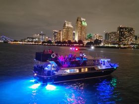 A vibrant party boat lights up the night as guests enjoy the stunning city skyline of San Diego — perfect for evening celebrations and scenic cruises.