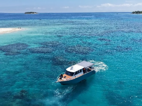 Aerial view of a boat navigating through crystal-clear waters, with a picturesque island in the background — perfect for exploring tropical destinations.