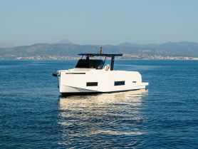 A sleek catamaran glides through calm waters, showcasing its modern design against a picturesque backdrop of mountains and coastline.