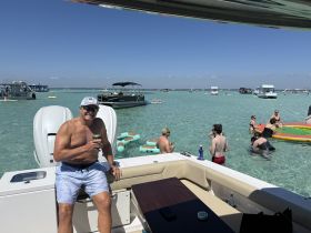 A lively scene of friends enjoying a sunny day on the water, with swimming, drinks, and fun activities around the boat — perfect for summer outings.