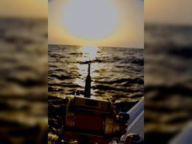 A close-up of a fishing reel against the backdrop of a stunning sunset over the ocean, highlighting the perfect setting for a fishing adventure.
