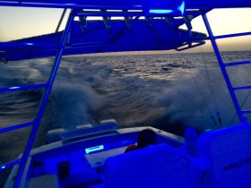 A view from the helm of a boat as it cuts through the waves, showcasing the interior seating and ambient blue lighting — perfect for evening cruises.