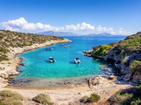 A stunning aerial view of a serene cove with multiple boats anchored in crystal-clear turquoise waters, surrounded by lush greenery and rocky shores — an ideal destination for boating adventures.