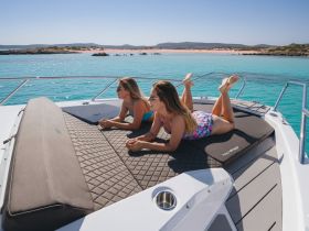 Two friends relax on the bow of a boat, enjoying the sun and stunning turquoise waters — a perfect day for leisure and fun on the water.