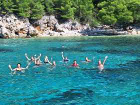 A lively group of friends enjoys a refreshing swim in crystal-clear waters, celebrating their day at the beach — perfect for summer adventures and group outings.