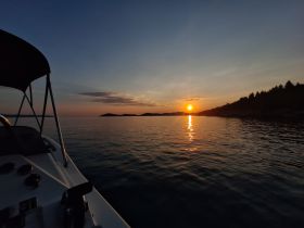 A serene sunset view from the deck of a boat, showcasing tranquil waters and distant islands — perfect for evening cruises.