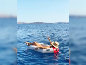 A woman relaxes on a floating mat in the serene waters, enjoying a drink with an island backdrop — the perfect summer getaway experience.