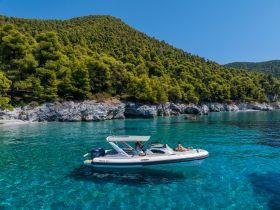A scenic view of a boat anchored in crystal-clear waters, with guests enjoying the sun and swimming along a beautiful coastline — perfect for summer adventures.
