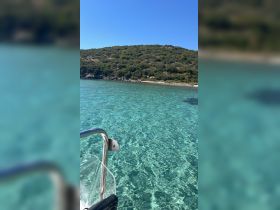 A serene view from a boat showcasing crystal-clear waters and a lush green shoreline, perfect for exploring hidden coves and enjoying nature.