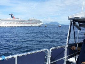 A scenic view of a cruise ship anchored in the ocean, with mountains in the background and a small boat in the foreground, showcasing the beauty of maritime adventures.