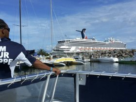 A scenic view of a cruise ship docked at a marina, with a boat in the foreground and a crew member visible, capturing the essence of a vibrant boating experience.