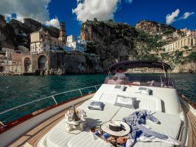 A scenic view of a man steering a boat along the stunning Amalfi Coast, showcasing beautiful cliffs and charming coastal architecture — perfect for exploring picturesque destinations.