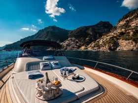 A luxurious lounge area on a yacht, featuring plush seating and refreshments, with stunning coastal views in the background — perfect for relaxing while cruising.