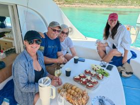 A joyful group enjoys a delightful meal aboard a yacht, complete with drinks and gourmet snacks, perfect for a relaxing day on the water.