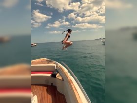 A woman leaps off the side of a boat into the sparkling water, capturing the essence of summer fun and adventure on the water.