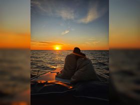 A couple enjoys a romantic sunset on a yacht, wrapped in blankets as the sun sets over the horizon — an idyllic moment for sunset cruises.