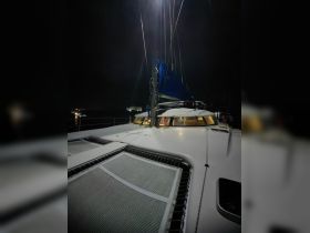 A sleek catamaran is illuminated under the night sky, showcasing its sails and deck — perfect for evening sailing adventures.