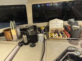 A well-equipped kitchen area inside a boat featuring a coffee maker, utensils, and storage for coffee capsules, perfect for onboard dining and comfort.