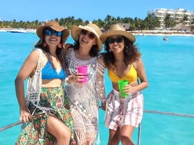Three friends enjoy a sunny day on a yacht, sipping colorful cocktails against a stunning turquoise backdrop — perfect for beach celebrations and memorable outings.