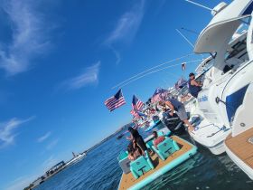 A lively group enjoys a fun day on the water, surrounded by multiple boats and American flags, perfect for summer celebrations and social gatherings.