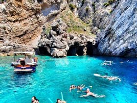 A lively group enjoys swimming and snorkeling in the stunning turquoise waters near a rocky cave, creating unforgettable memories in a picturesque setting.