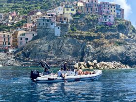 A scenic view of a group enjoying a boat ride along the stunning coastline of Cinque Terre, with colorful houses perched on the cliffs — a perfect summer adventure.