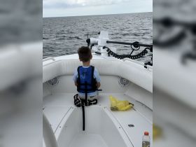 A young boy sits in a boat's interior, wearing a life jacket and gazing out at the water, showcasing a safe and enjoyable boating experience for families.