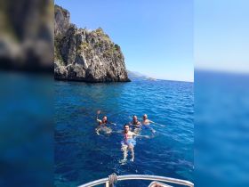 A lively group enjoys a refreshing swim in crystal-clear waters near a stunning rocky coastline, perfect for summer adventures and memorable outings.