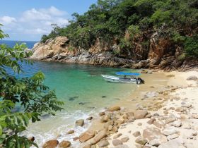 A serene view of a boat docked on a sandy beach, surrounded by lush greenery and rocky cliffs — a perfect spot for relaxation and exploration.
