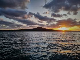 A stunning sunset over a tranquil waterway, with a silhouette of an island in the background, perfect for capturing the beauty of nature during a boat trip.