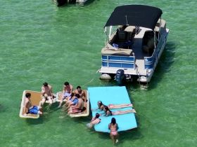 A lively group enjoys a fun day on the water, relaxing on floating mats and a pontoon boat, perfect for summer parties and aquatic adventures.