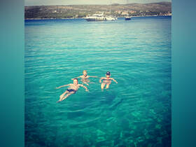 Three friends enjoy a refreshing swim in the crystal-clear waters, with a beautiful yacht anchored in the background — a perfect summer getaway.
