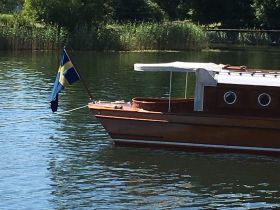 A beautifully crafted wooden boat is docked peacefully, showcasing its elegant design and the Swedish flag fluttering in the breeze.
