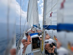 A lively group enjoys a relaxing day sailing, lounging on the deck of a sailboat under the sun — perfect for summer adventures on the water.