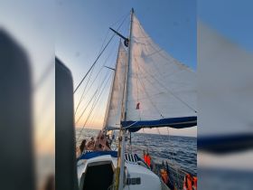 A lively group enjoys a sailing experience at sunset, capturing the essence of adventure on the open ocean.