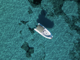 Aerial view of a sleek speedboat gliding over crystal-clear waters, showcasing the vibrant underwater landscape — perfect for exploring coastal destinations.