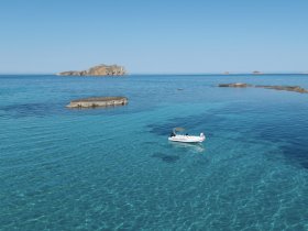 An aerial view of a boat navigating through crystal-clear turquoise waters, with a picturesque island in the background — a perfect scene for exploring beautiful coastal destinations.
