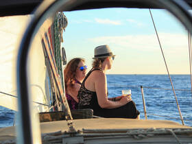 A couple enjoys drinks while watching the sunset from the deck of a sailboat, creating a perfect romantic atmosphere on the water.