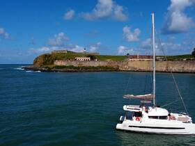 A catamaran sails near a historic coastal fort, showcasing stunning scenery and a perfect day on the water.