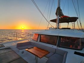 A serene sunset view from the deck of a catamaran, showcasing the tranquil waters and the vibrant colors of the sky — perfect for romantic evening cruises.