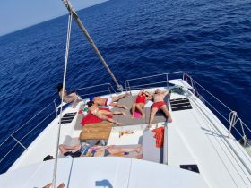 A group of friends relaxes and sunbathes on the deck of a catamaran, enjoying the beautiful ocean views — perfect for a day of leisure on the water.