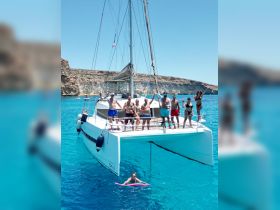 A lively group celebrates aboard a catamaran in crystal-clear waters, enjoying swimming and fun under the sun — perfect for summer adventures.