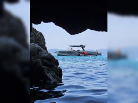 A stunning view of a boat anchored near a rocky cave, with people enjoying the water — a perfect summer getaway for adventure seekers.