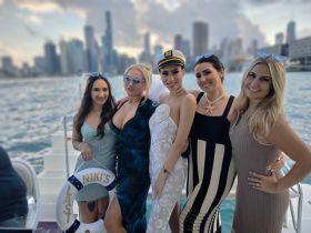 A group of friends celebrates a bachelorette party aboard a boat, showcasing smiles and fun against a stunning city skyline backdrop.