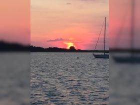 A serene sunset view featuring a sailboat silhouetted against vibrant hues of orange and pink, perfect for capturing the beauty of evening on the water.