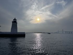 A stunning sunset view featuring a lighthouse and a bridge, with a boat cruising in the foreground — a picturesque moment capturing the beauty of the waterway.